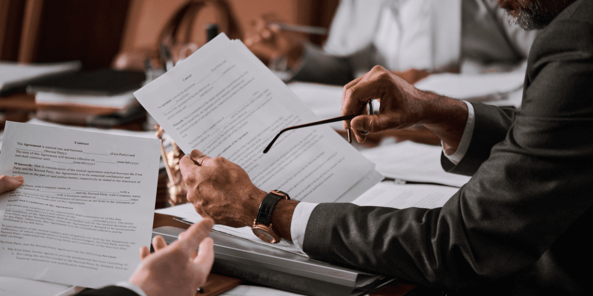 A person in a suit reviewing documents while holding glasses in a meeting setting