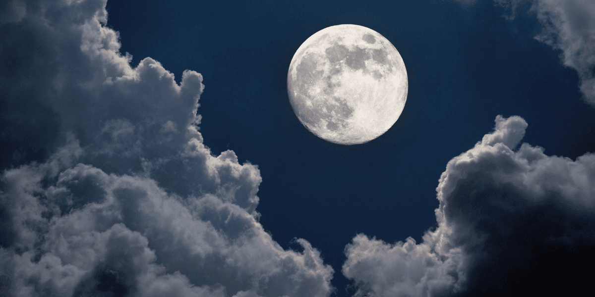 A bright moon illuminated against a dark sky filled with fluffy clouds