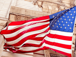 American flag waving outside an ornate stone government building.