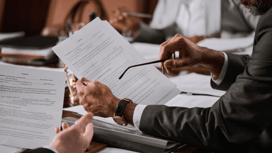 A person in a suit reviewing documents while holding glasses in a meeting setting