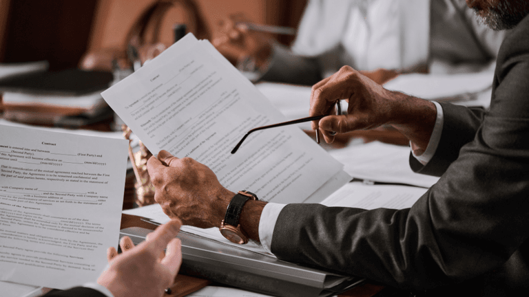 A person in a suit reviewing documents while holding glasses in a meeting setting