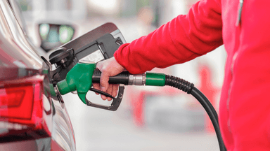 Person in a red jacket fueling a car at a gas station.