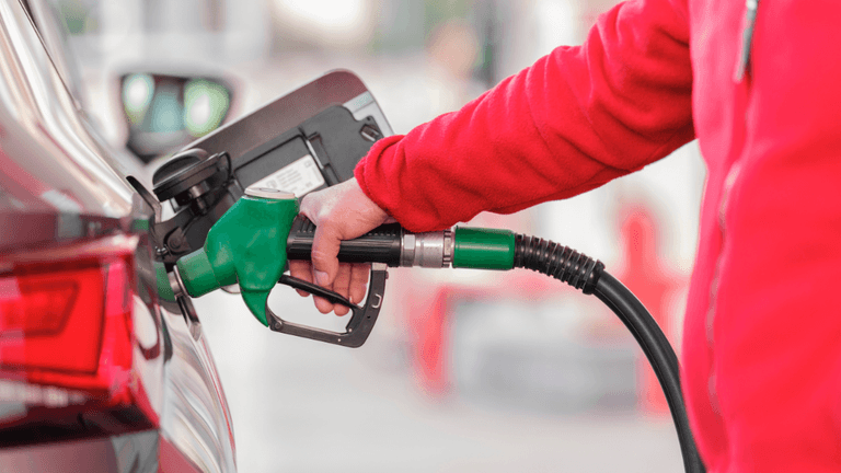 Person in a red jacket fueling a car at a gas station.