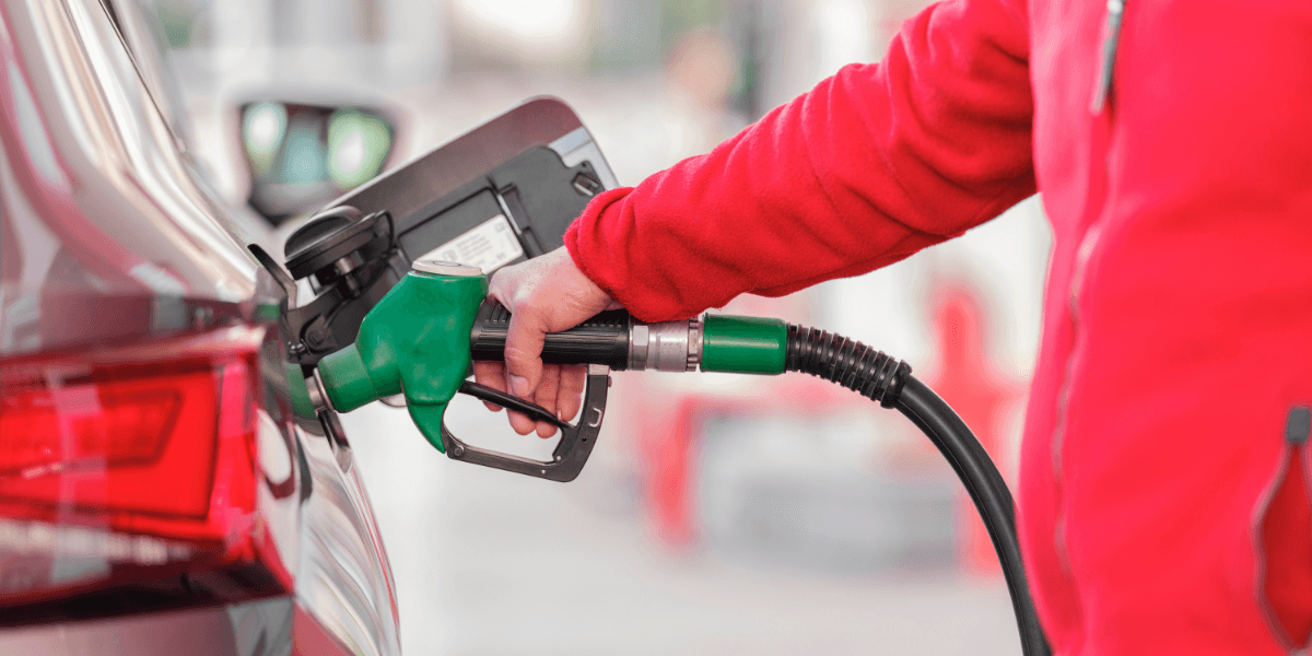 Person in a red jacket fueling a car at a gas station.