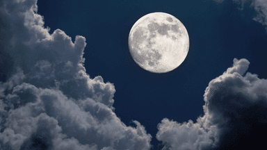 A bright moon illuminated against a dark sky filled with fluffy clouds