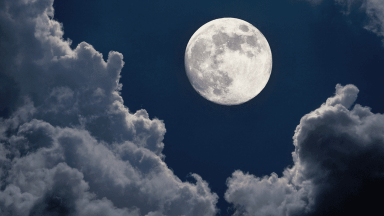 A bright moon illuminated against a dark sky filled with fluffy clouds