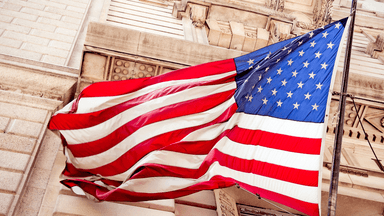 American flag waving outside an ornate stone government building.