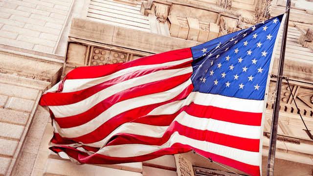 American flag waving outside an ornate stone government building.