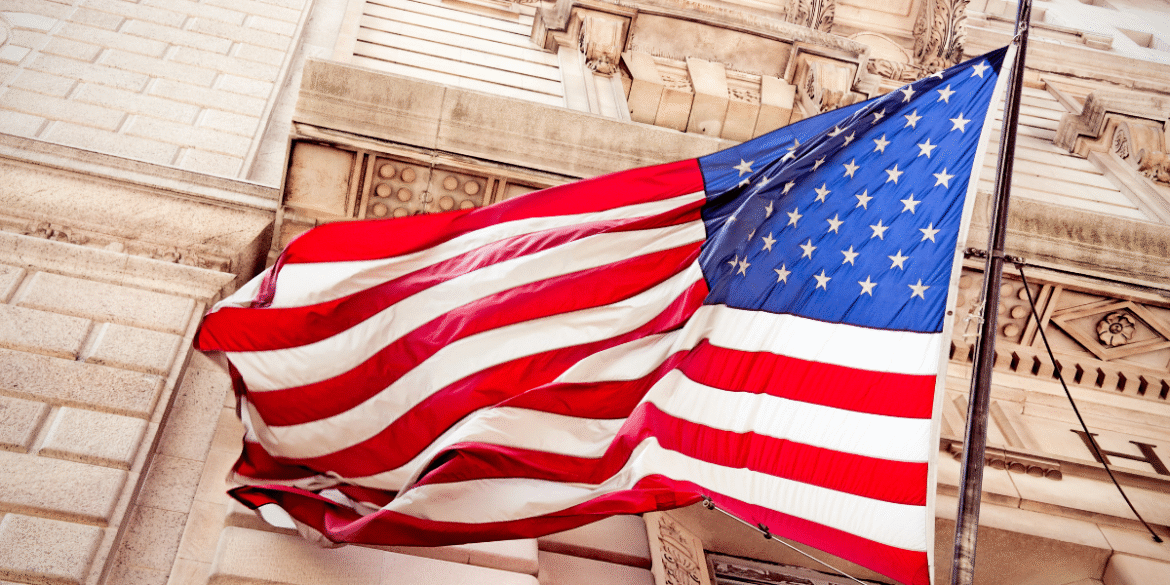 American flag waving outside an ornate stone government building.